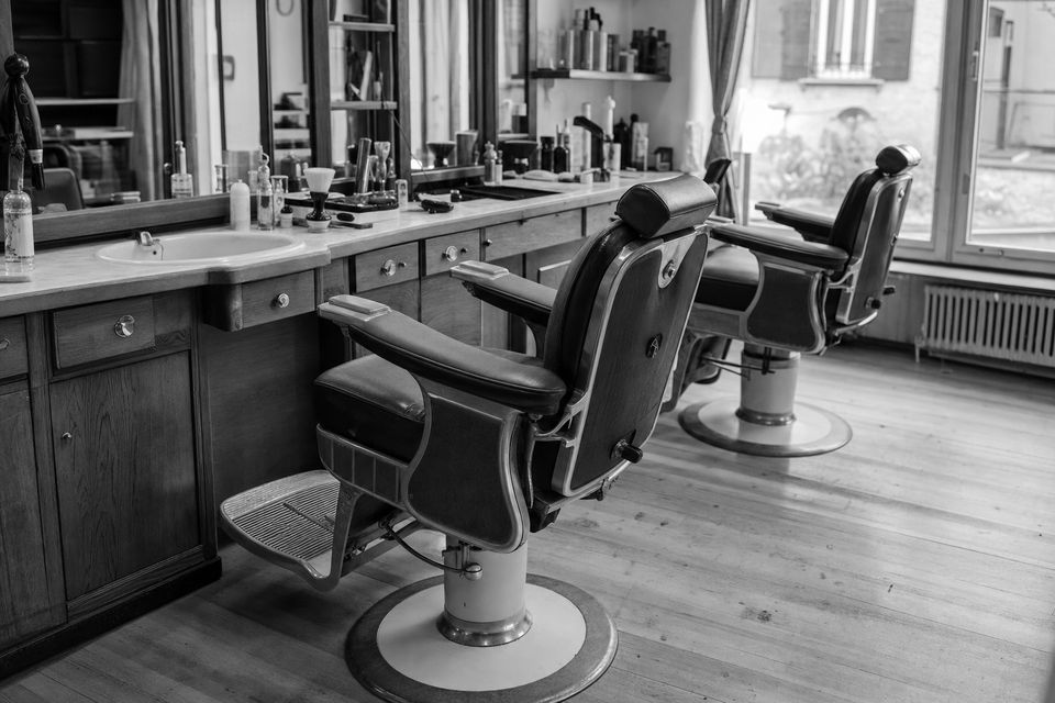 Schwarz-weißes Stimmungsbild: einzelner Frisierstuhl vor großem Spiegel in einem ruhigen Salonraum